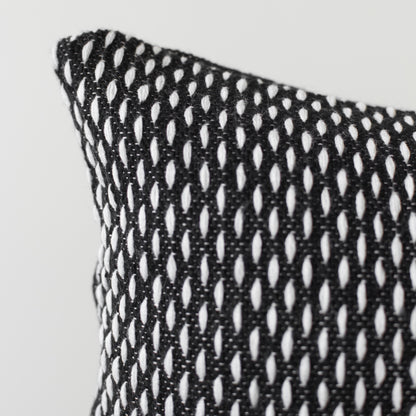 Black and white open-weave lumbar pillow with repeating oval cutout pattern and visible corner edge detail.