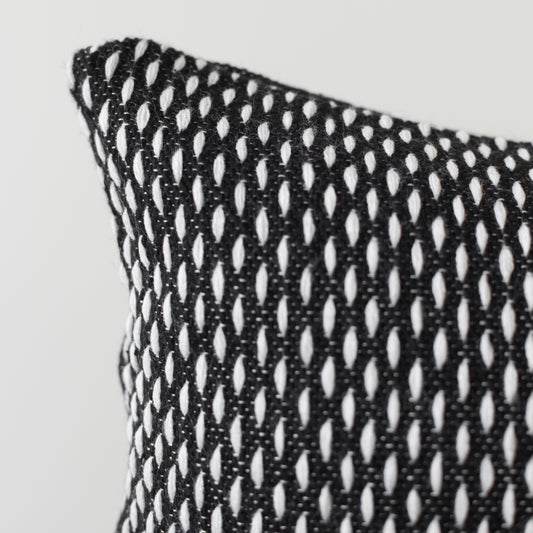 Black and white open-weave lumbar pillow with repeating oval cutout pattern and visible corner edge detail.