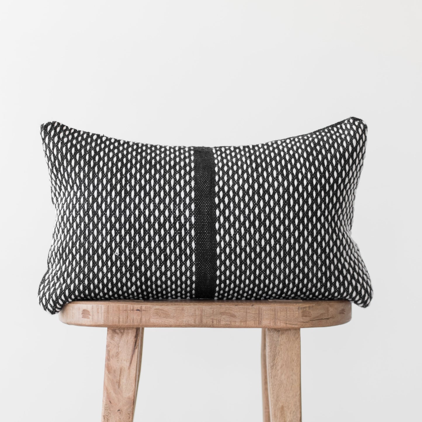 Black and white woven lumbar pillow with vertical stripe detail on wooden chair.
