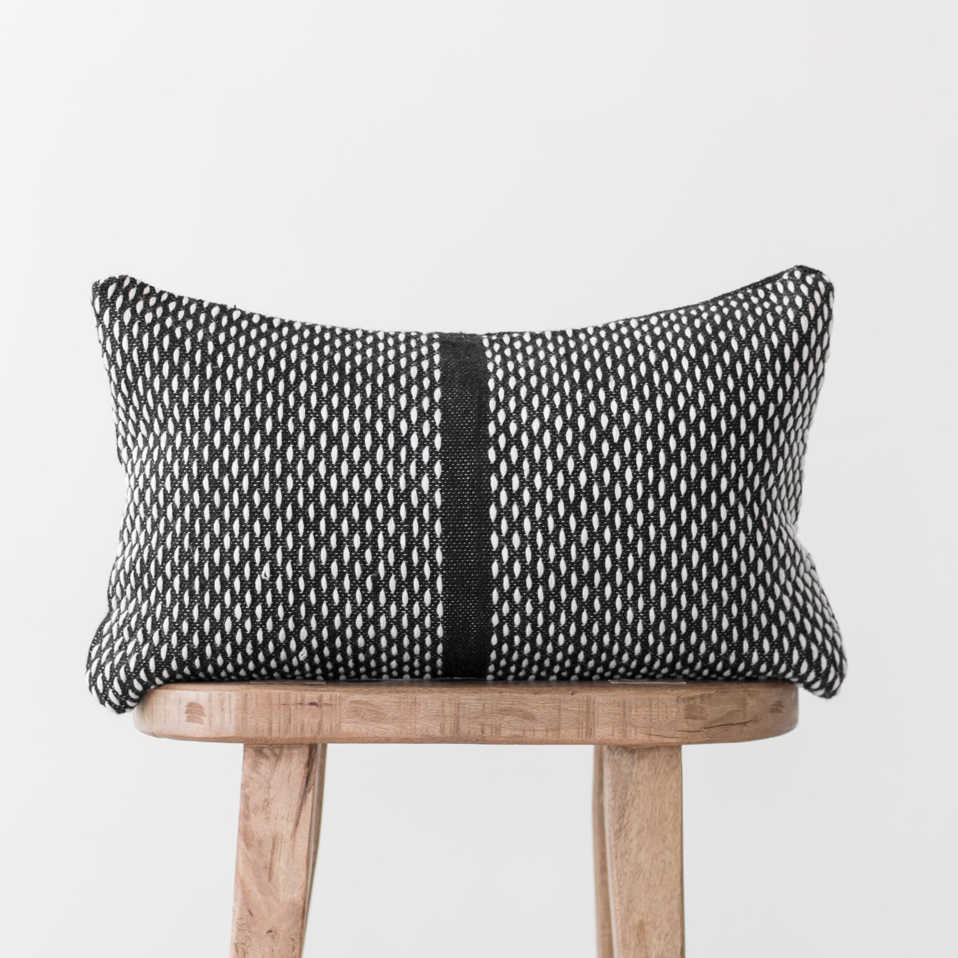 Black and white woven lumbar pillow with vertical stripe detail on wooden chair.