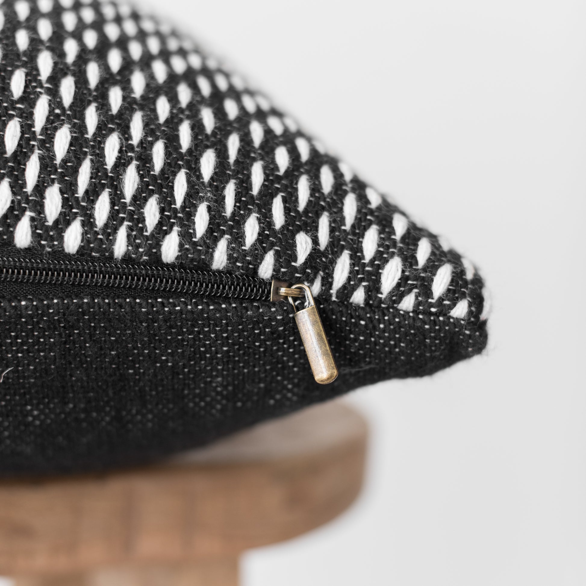 Black and white patterned lumbar pillow with gold zipper detail on woven textile.