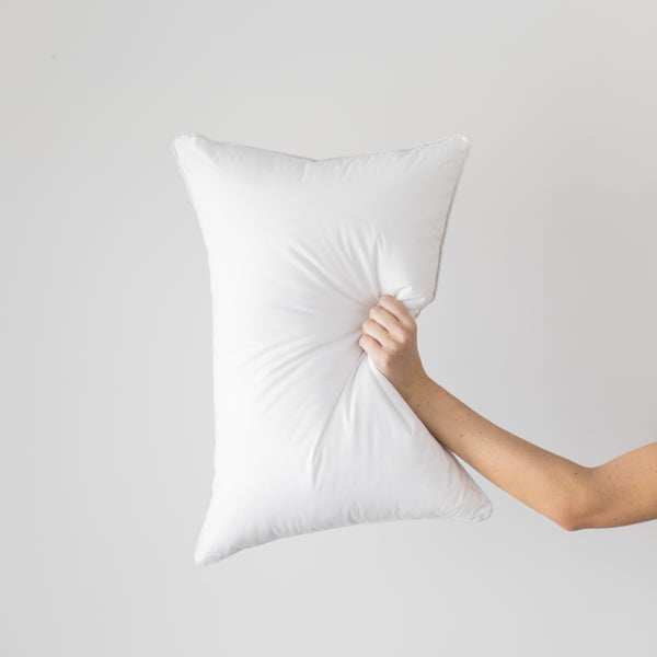 White rectangular pillow insert held in hand, showing soft, puffy fill and smooth fabric cover.