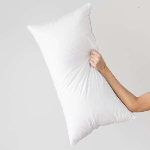 White rectangular pillow insert held by hand against gray background.