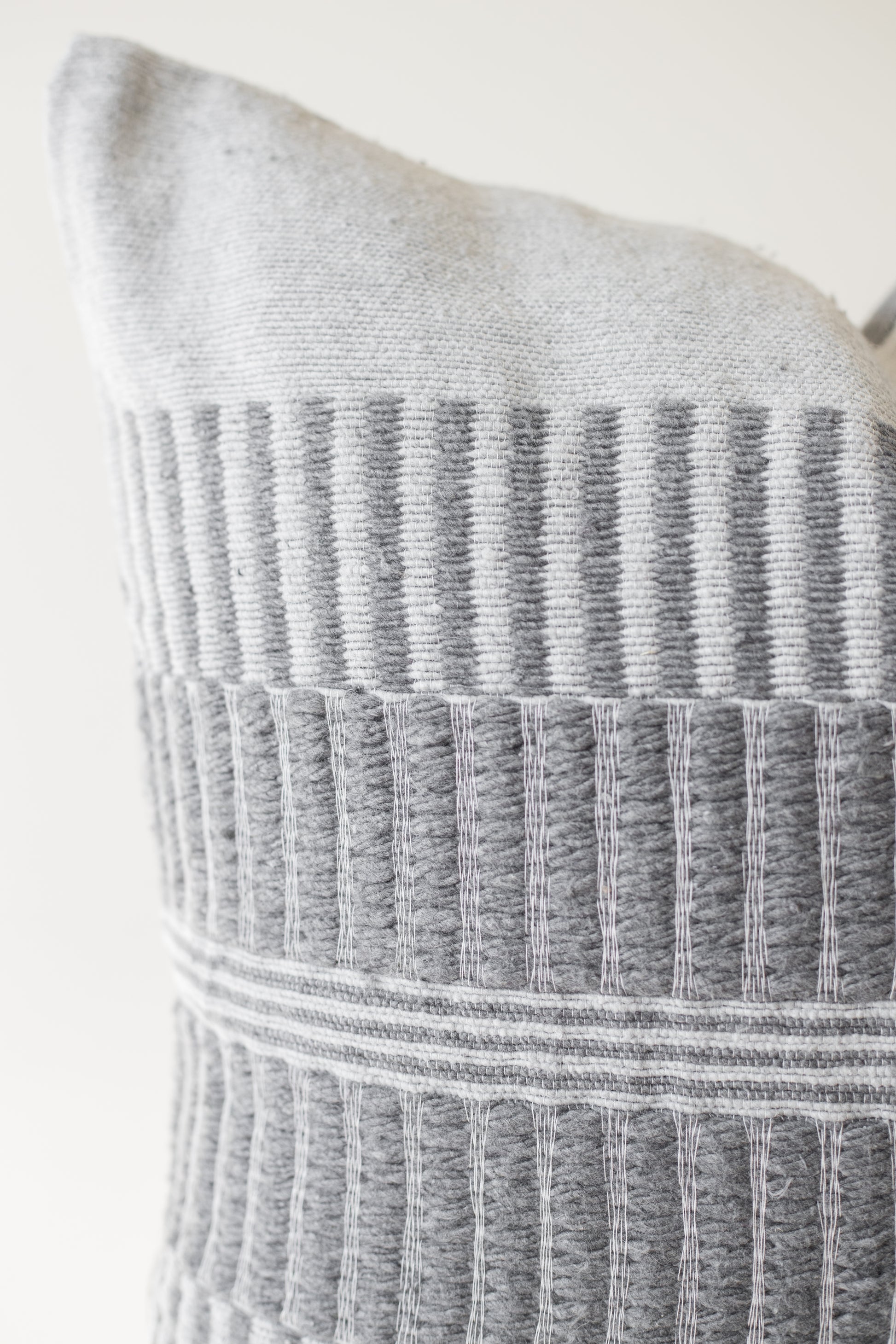 Gray and white woven pillow with vertical striped pattern and horizontal bands across center section.