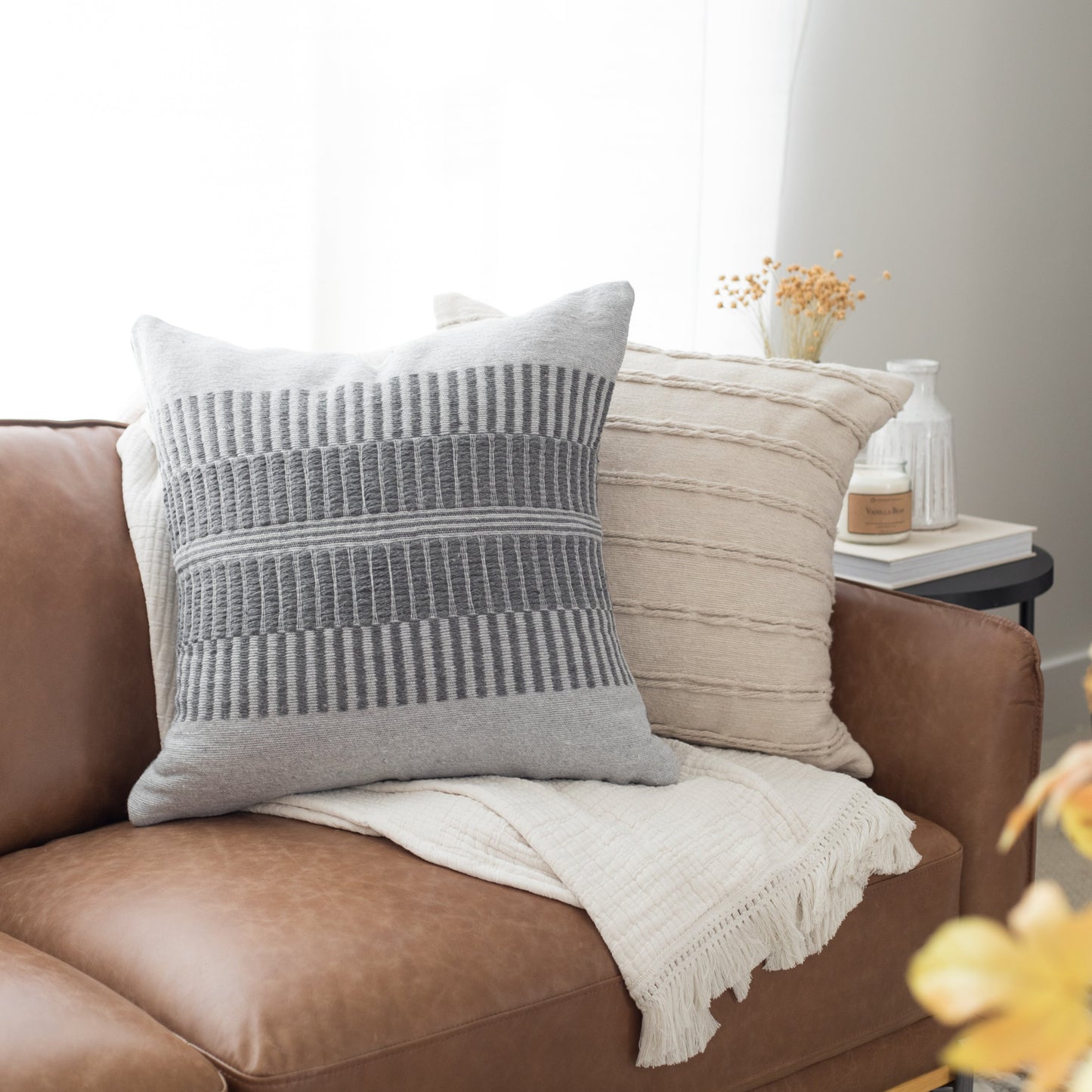Gray and cream striped pillows arranged on a brown leather chair with a cream throw blanket.