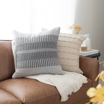 Gray and cream striped pillows arranged on a brown leather chair with a cream throw blanket.