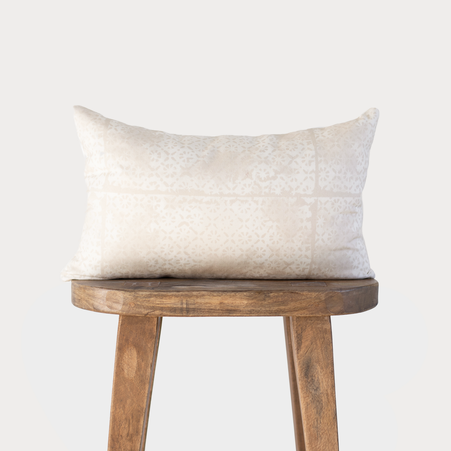 Cream rectangular pillow with faded floral pattern displayed on wooden stool.