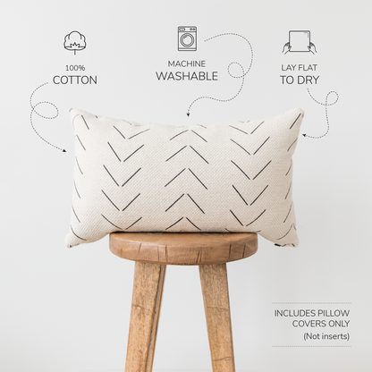 Cream lumbar pillow cover with geometric chevron pattern in charcoal, displayed on wooden stool.