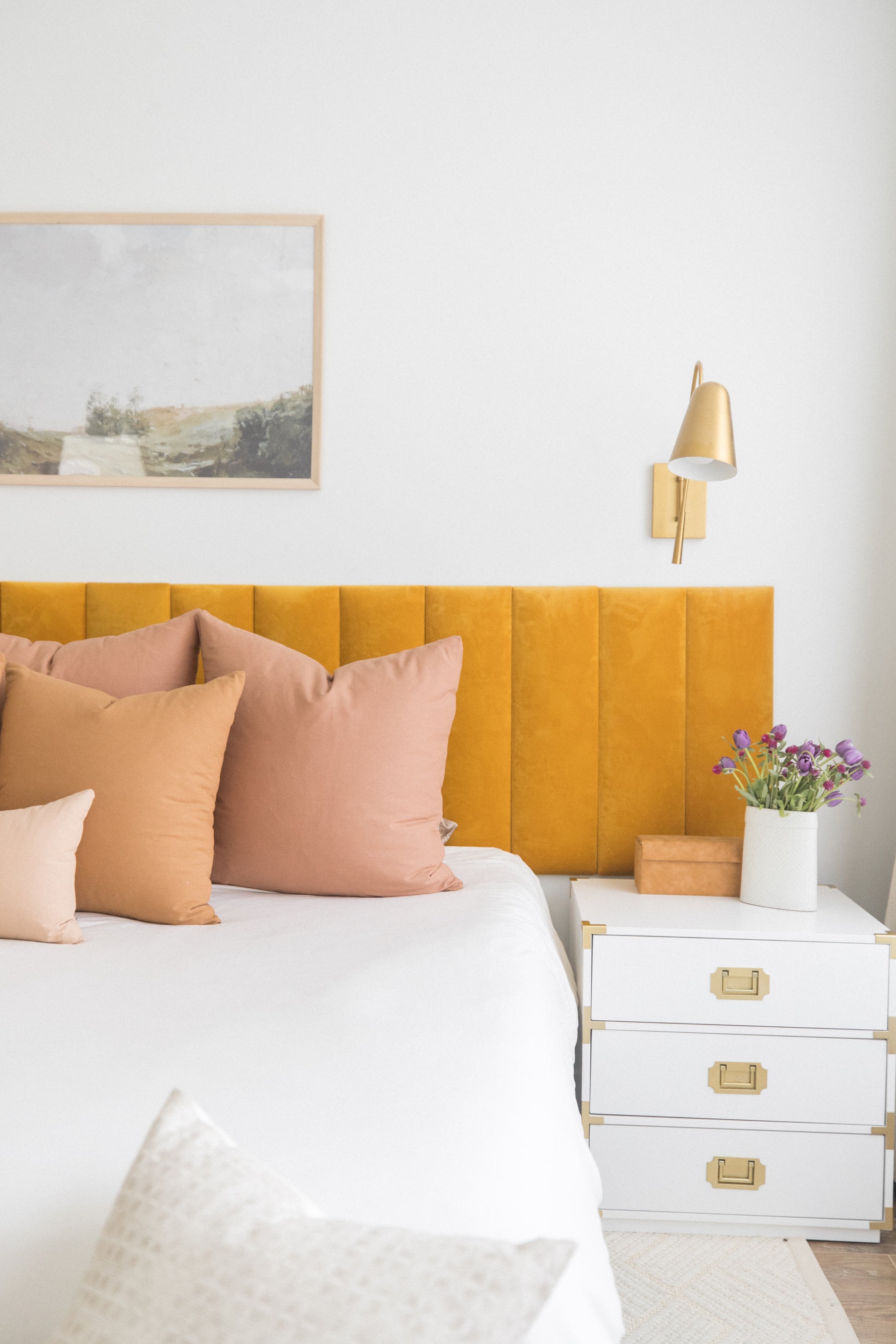 Dusty rose and tan square throw pillows arranged on a bed with yellow headboard and white bedding.