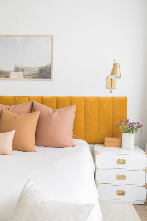 Dusty rose and tan square throw pillows arranged on a bed with yellow headboard and white bedding.