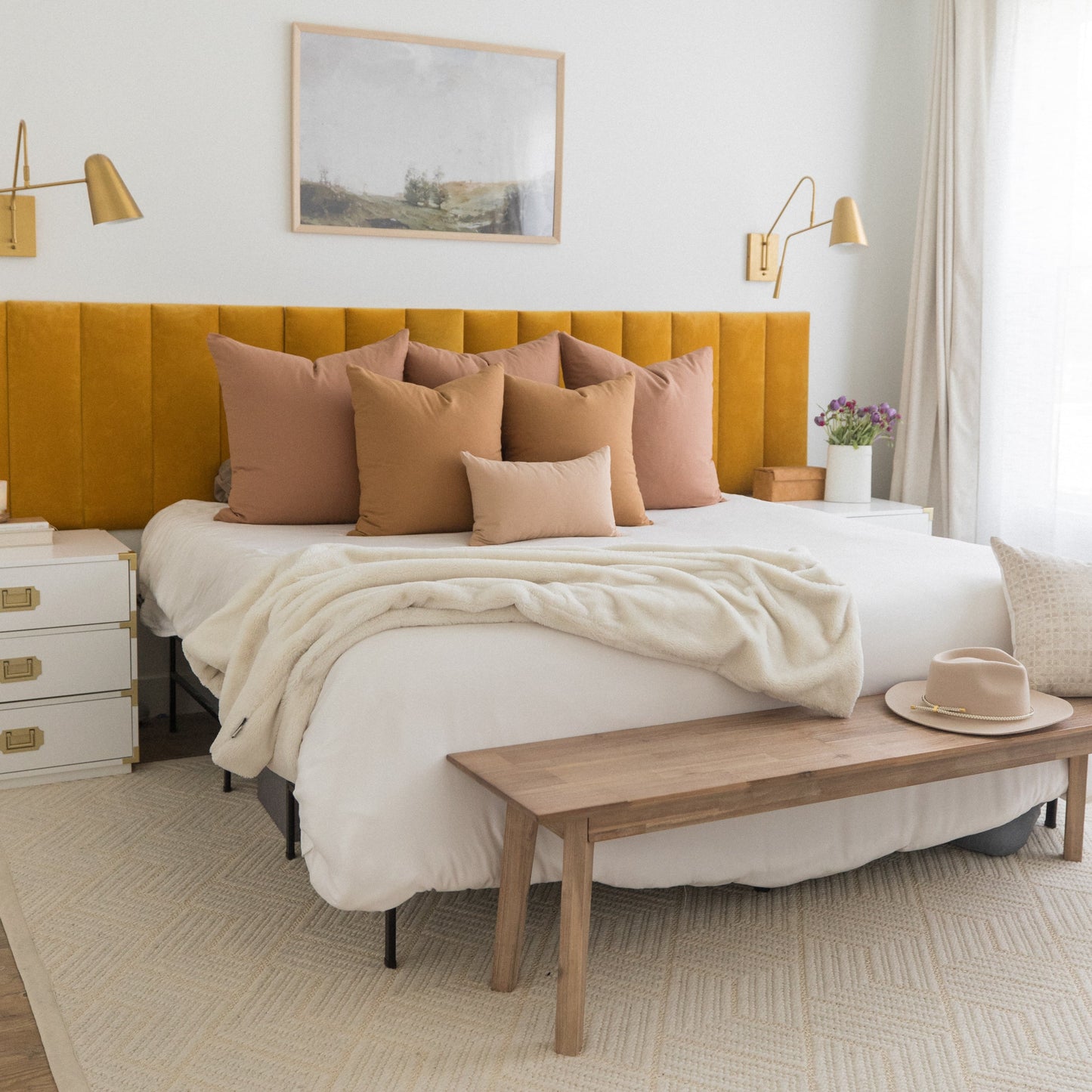 Mustard yellow upholstered headboard with tan and blush decorative pillows on a bed with cream bedding.