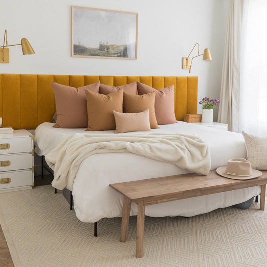 Mustard yellow upholstered headboard with tan and blush decorative pillows on a bed with cream bedding.