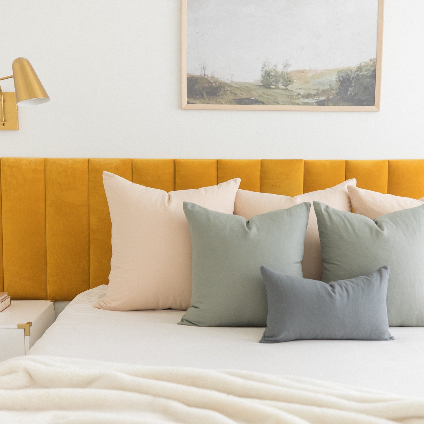 Bed styled with sage green and cream pillows in various sizes against a mustard yellow upholstered headboard.