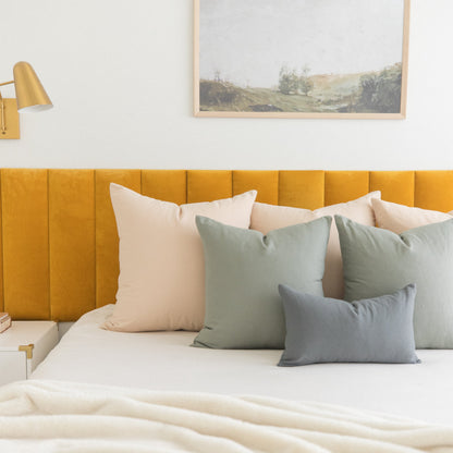 Bed styled with sage green and cream pillows in various sizes against a mustard yellow upholstered headboard.