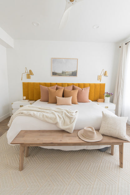 Dusty rose and tan throw pillows arranged on a bed with yellow headboard in a modern bedroom.