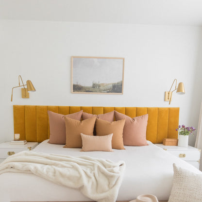 Terracotta-colored pillows arranged on a bed with mustard yellow headboard and white bedding.