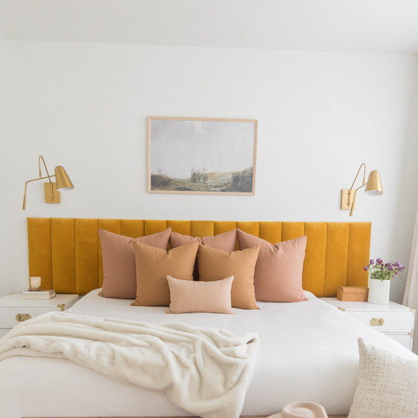 Terracotta-colored pillows arranged on a bed with mustard yellow headboard and white bedding.