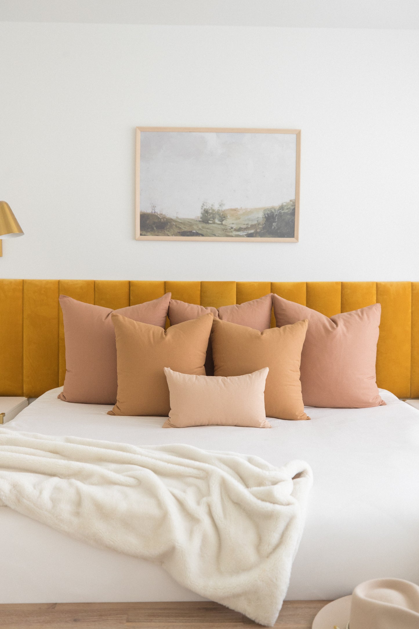 Multiple dusty rose and tan throw pillows arranged on a bed with yellow upholstered headboard.