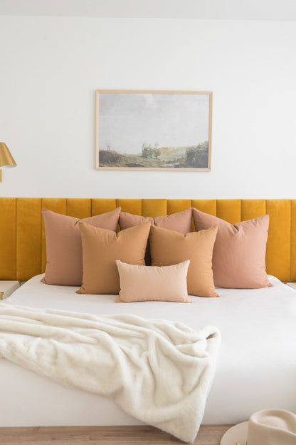 Multiple dusty rose and tan throw pillows arranged on a bed with yellow upholstered headboard.
