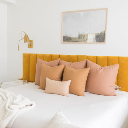 Five terracotta and peach-toned pillows arranged on a bed with yellow upholstered headboard.