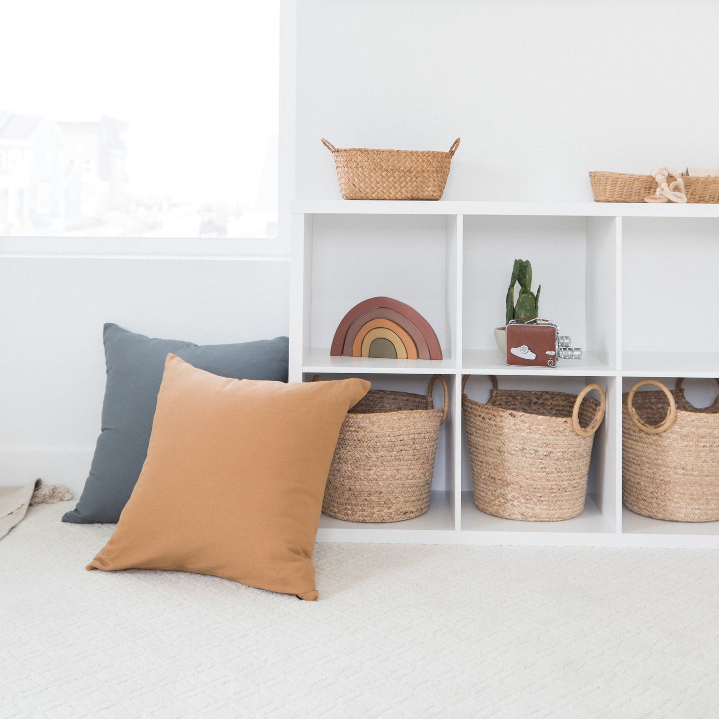 Tan and blue throw pillows displayed on white shelving with woven baskets and decorative items.