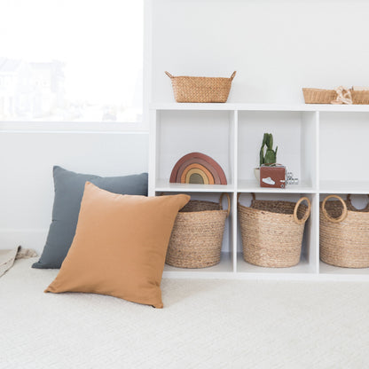 Tan and blue throw pillows displayed on white shelving with woven baskets and decorative items.