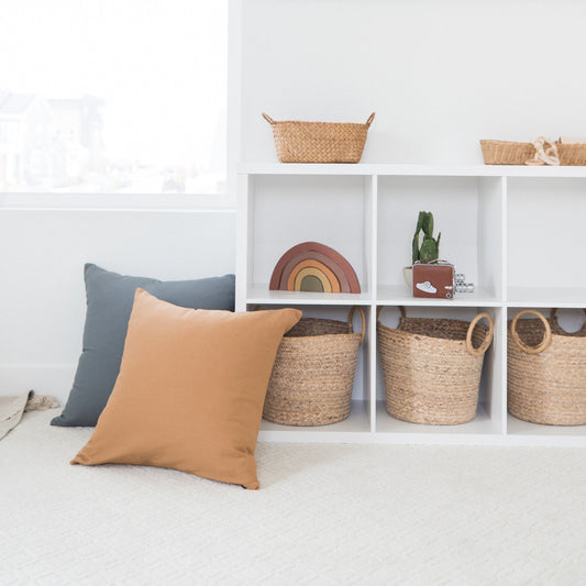Tan and blue throw pillows displayed on white shelving with woven baskets and decorative items.