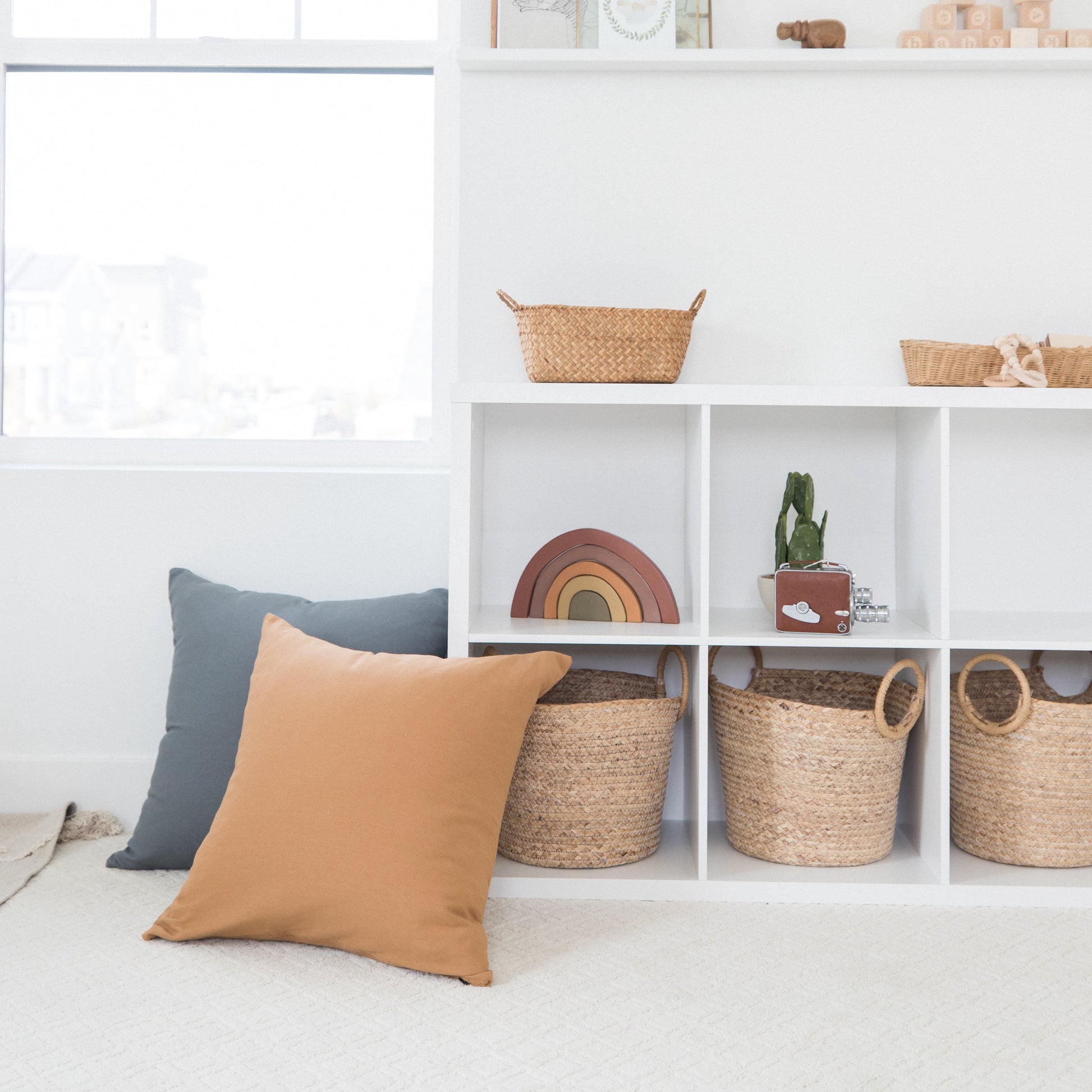 Terracotta-colored square pillow displayed on white shelving with woven baskets and decor.