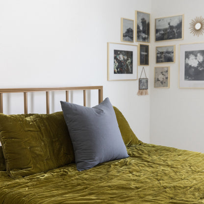 Gray square pillow displayed on a bed with olive green bedding and wooden frame headboard.