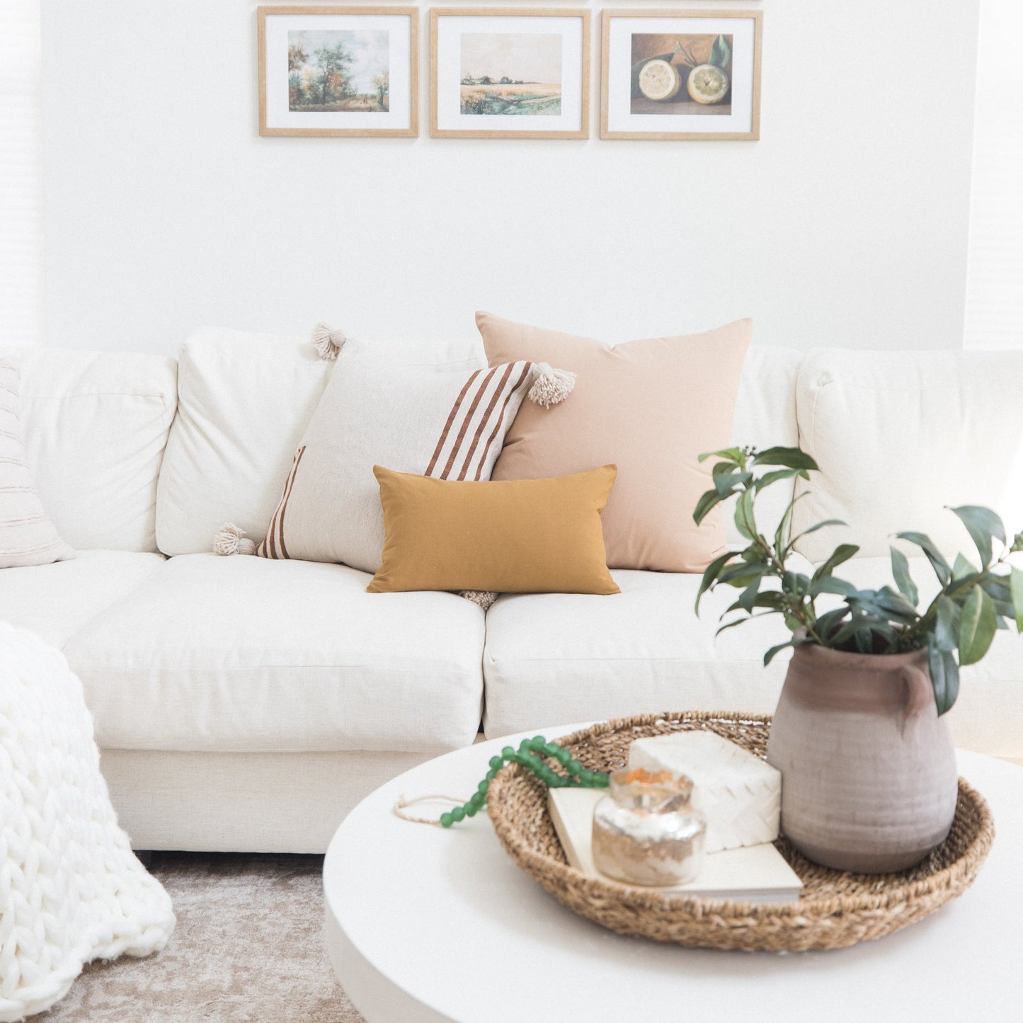 Three framed artworks with natural wood frames displayed above a white sofa with decorative pillows.