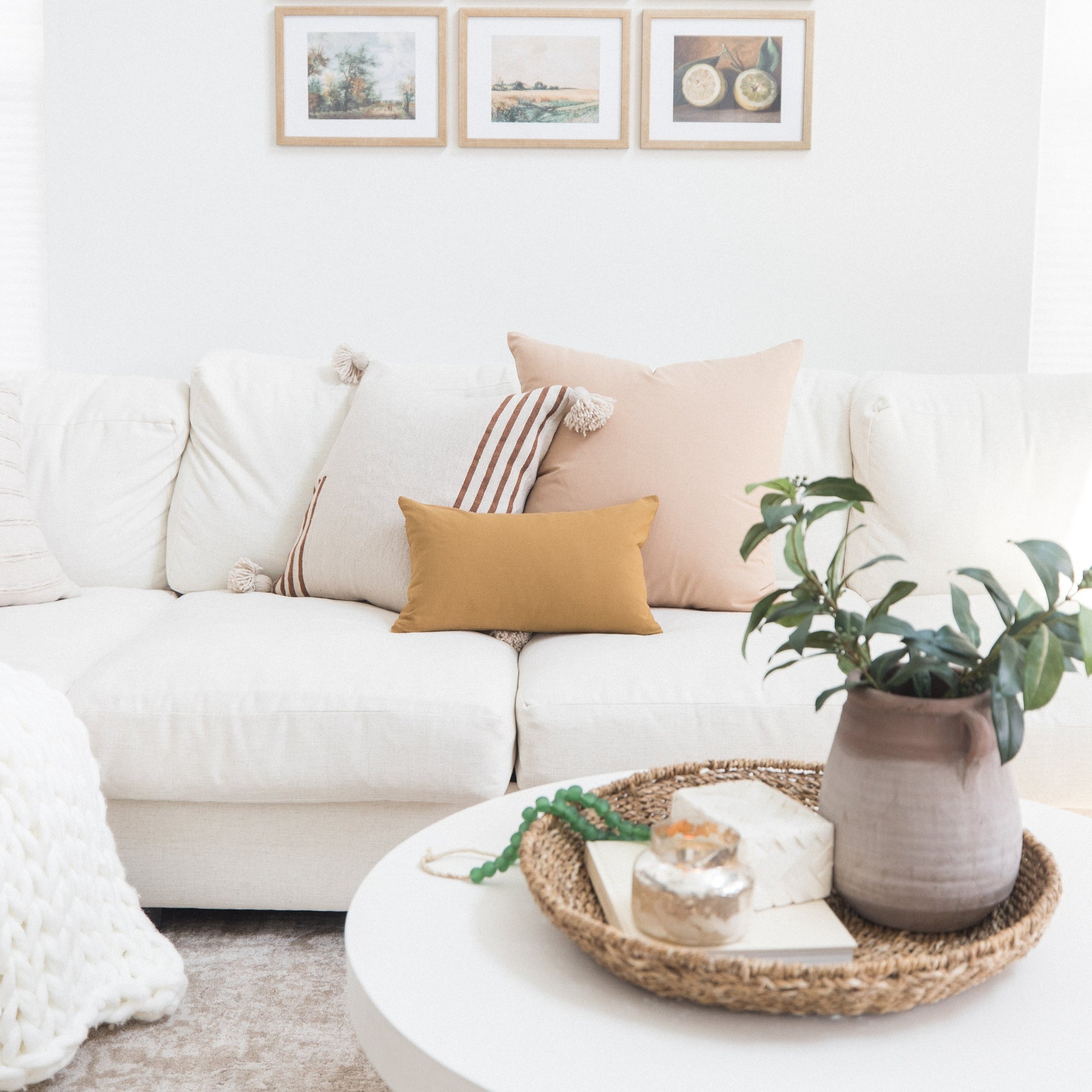 Three framed artworks with natural wood frames displayed above a white sofa with decorative pillows.