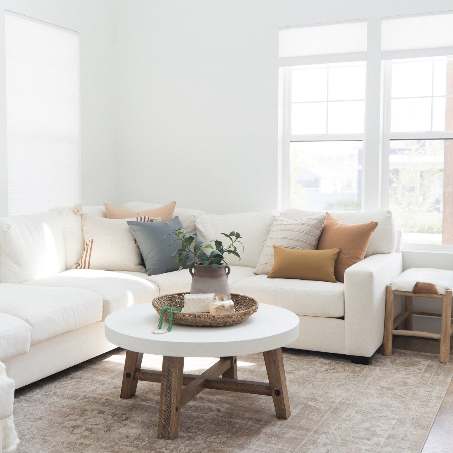 White round coffee table with natural wood base in bright living room with cream sectional sofa.