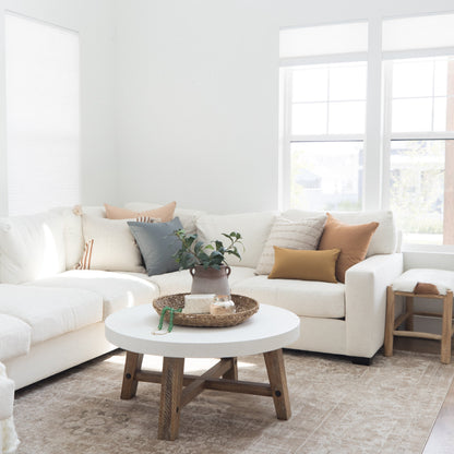 White round coffee table with natural wood base in bright living room with cream sectional sofa.