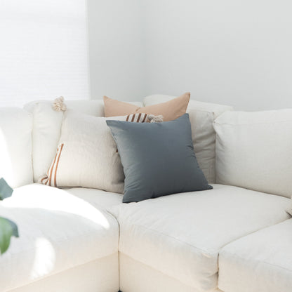 Decorative pillows in blue, tan, and cream with striped details arranged on a white upholstered sofa.
