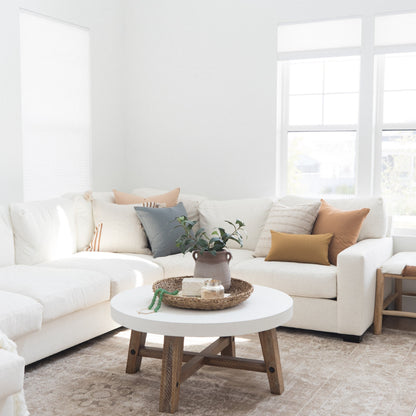 White upholstered sectional sofa with curved design, layered with neutral and earth-toned pillows in a bright living room.
