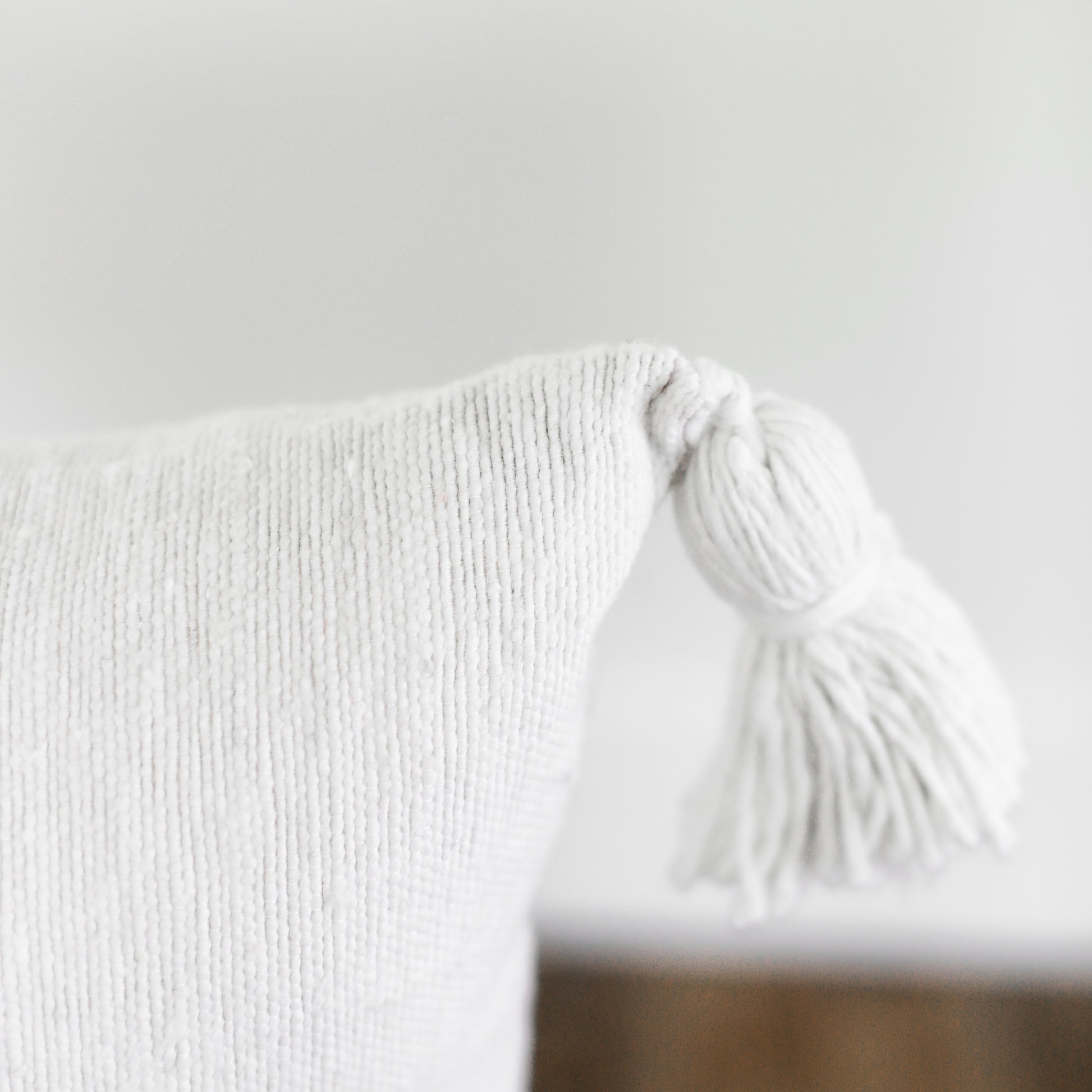 White lumbar pillow with ribbed texture and tassel trim detail.