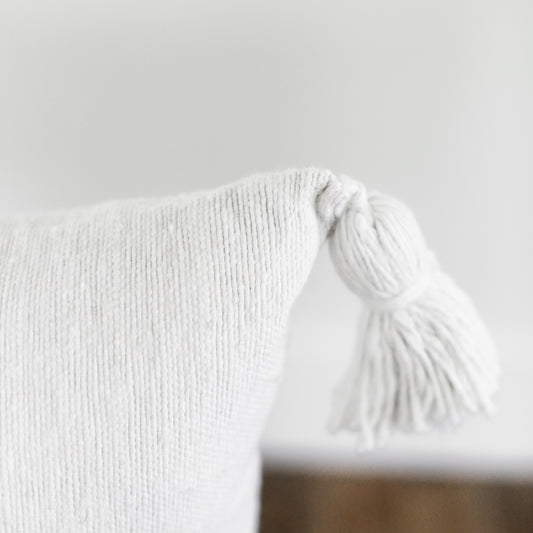 White lumbar pillow with ribbed texture and tassel trim detail.