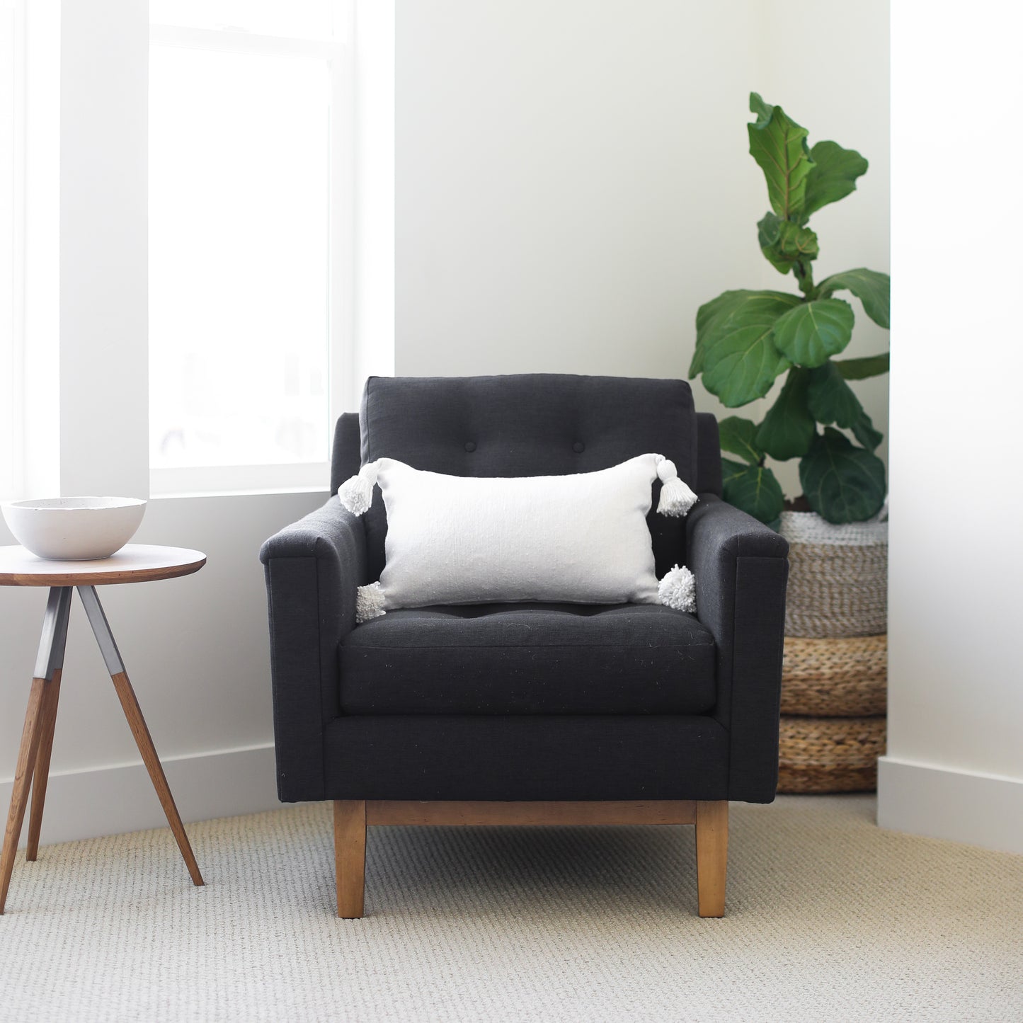 White lumbar pillow with tassel corners displayed on a dark gray upholstered armchair.