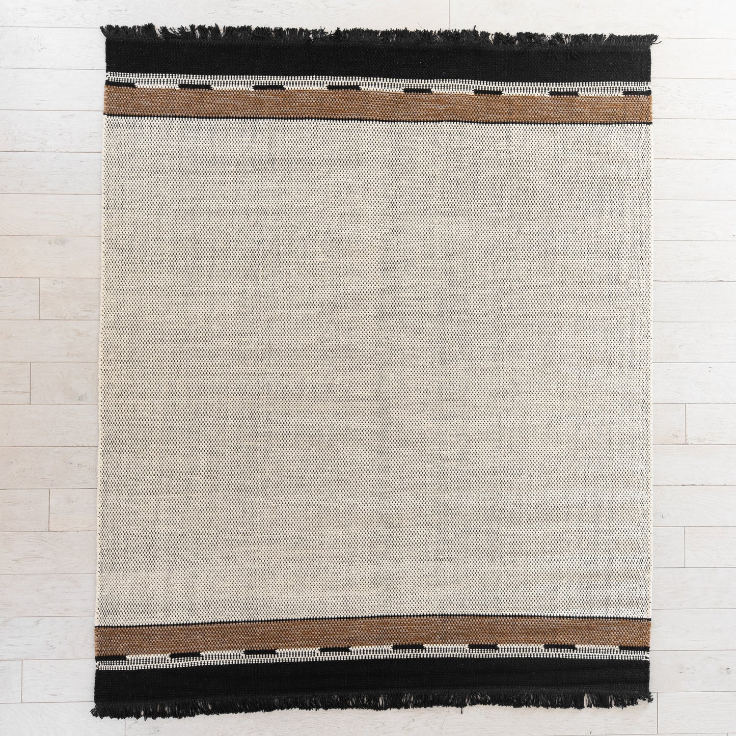 Flat-woven rug with cream center, brown and white striped borders, and black fringe on top and bottom edges.