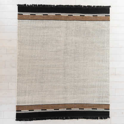 Flat-woven rug with cream center, brown and white striped borders, and black fringe on top and bottom edges.