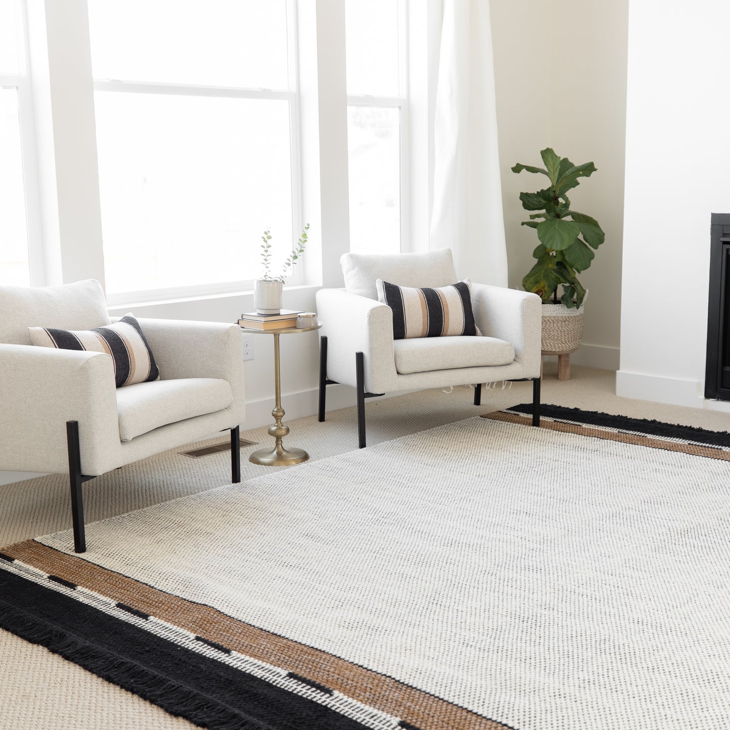 Cream upholstered armchair with black legs and striped accent pillow in modern living room setting.