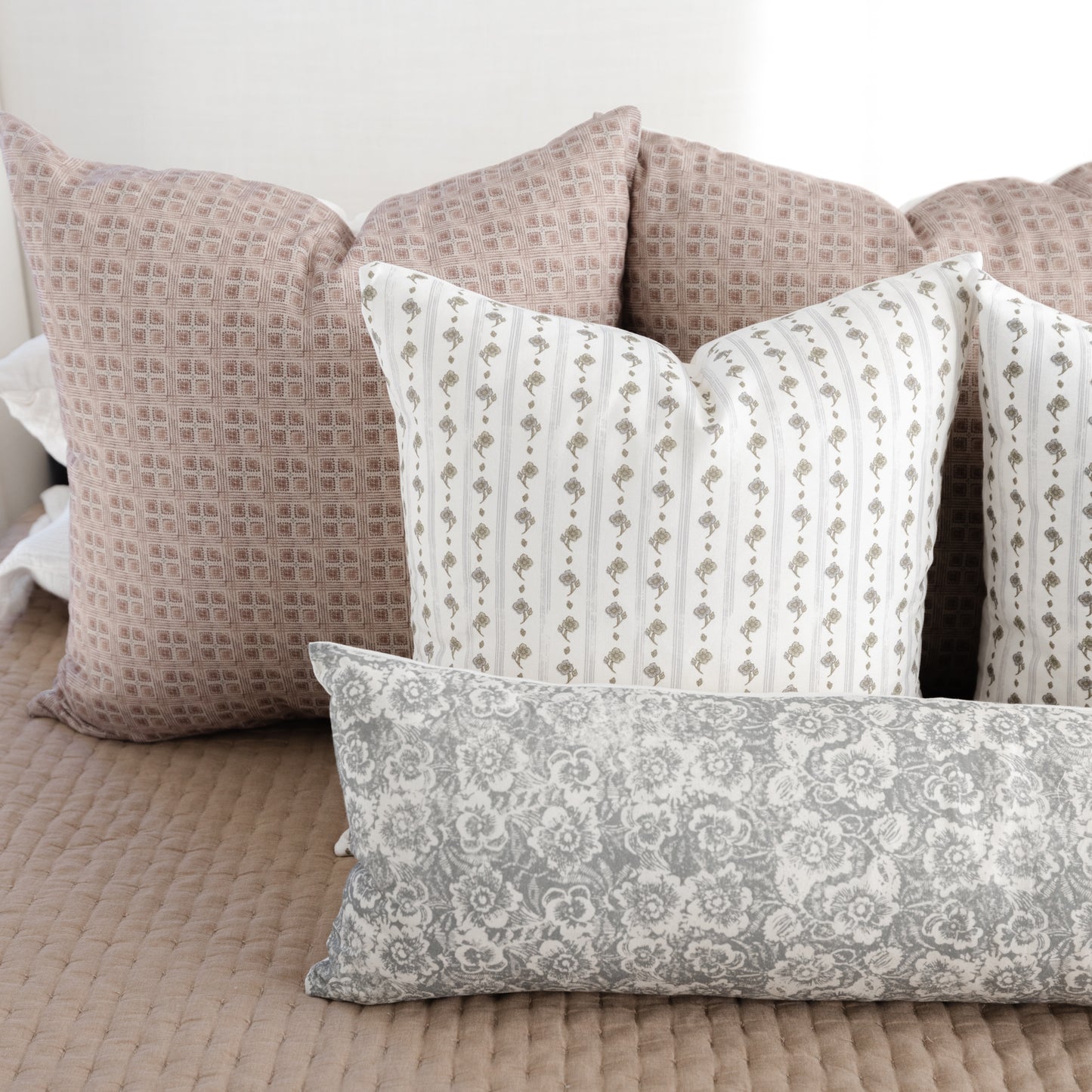 Gray lumbar pillow with floral damask pattern displayed among coordinating decorative pillows on a bed.