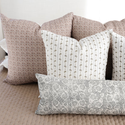 Gray lumbar pillow with floral damask pattern displayed among coordinating decorative pillows on a bed.