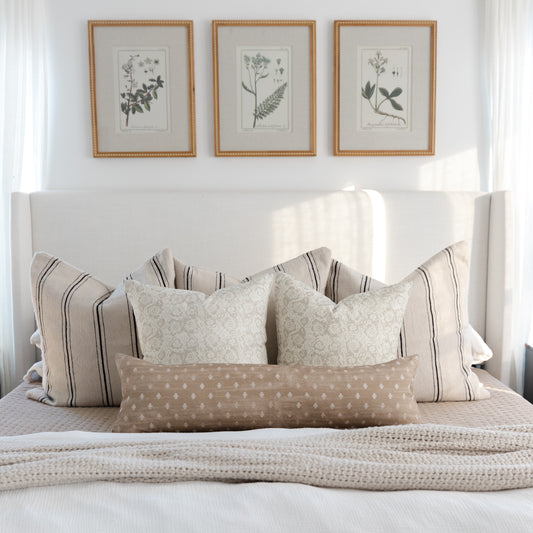 Rectangular lumbar pillow with tan and white polka dot pattern displayed on bed with striped pillows.