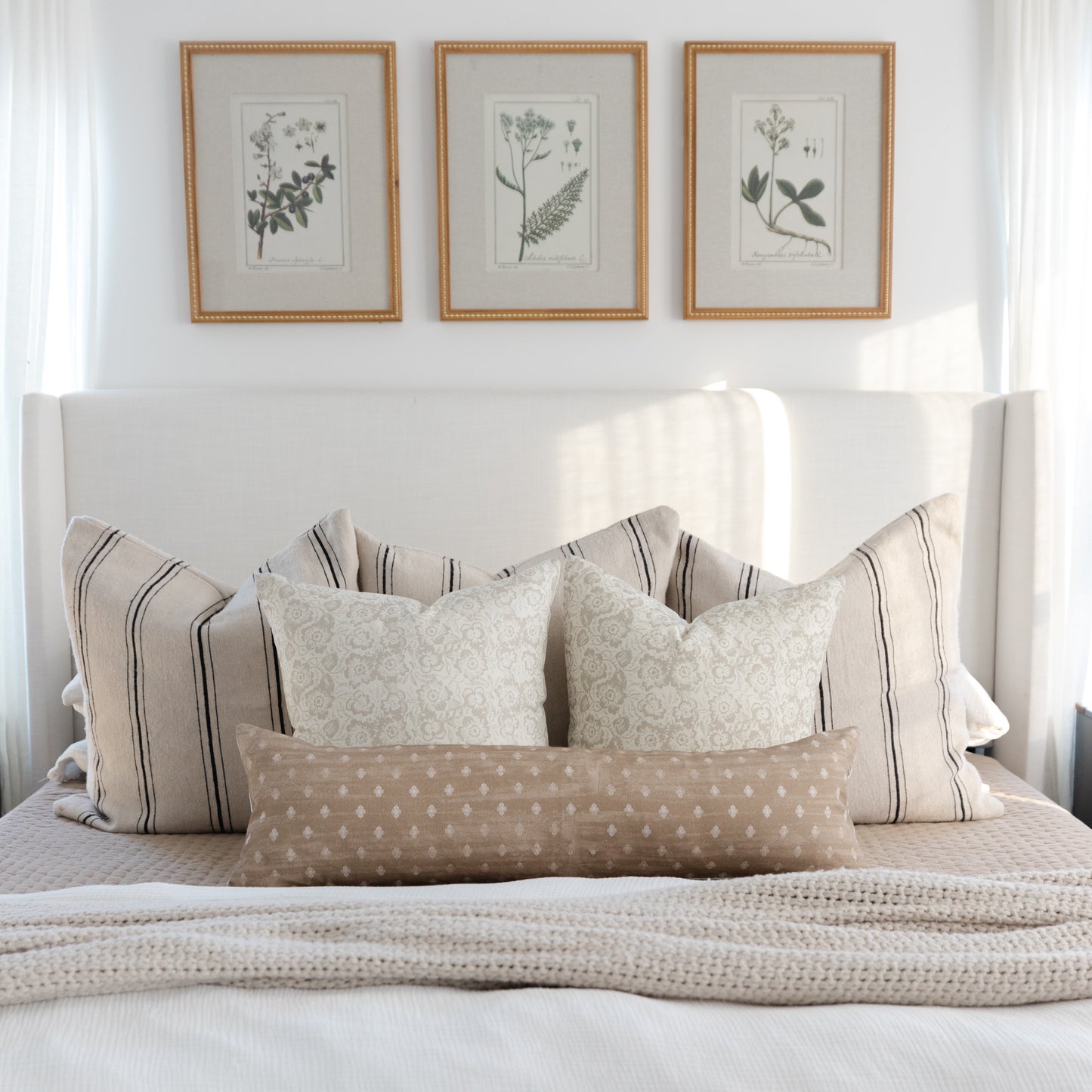 Cream pillow cover with subtle botanical damask pattern, displayed on bed with striped and patterned coordinating pillows.