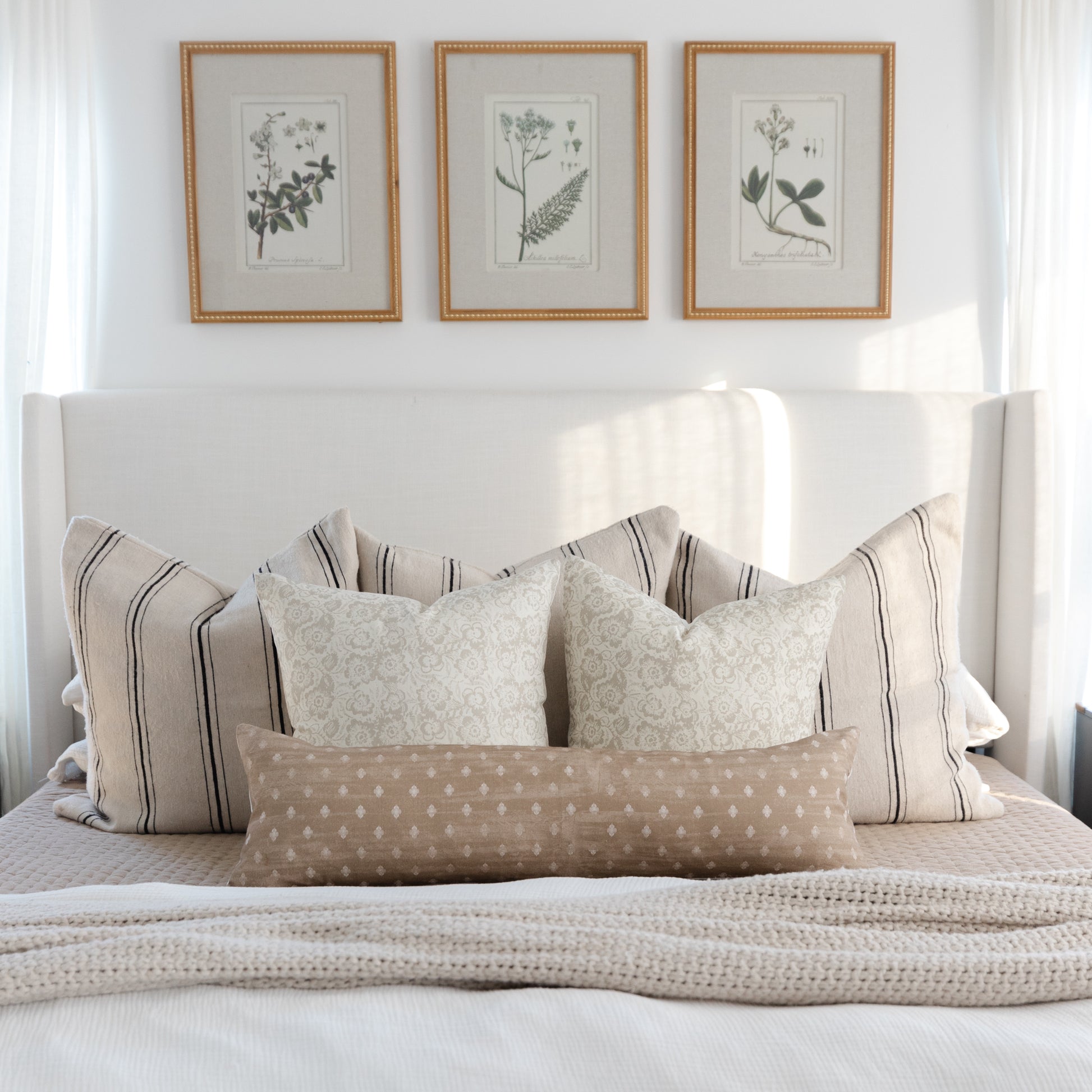 Cream pillow cover with subtle botanical damask pattern, displayed on bed with striped and patterned coordinating pillows.