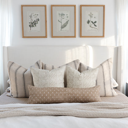 Cream pillow cover with subtle botanical damask pattern, displayed on bed with striped and patterned coordinating pillows.