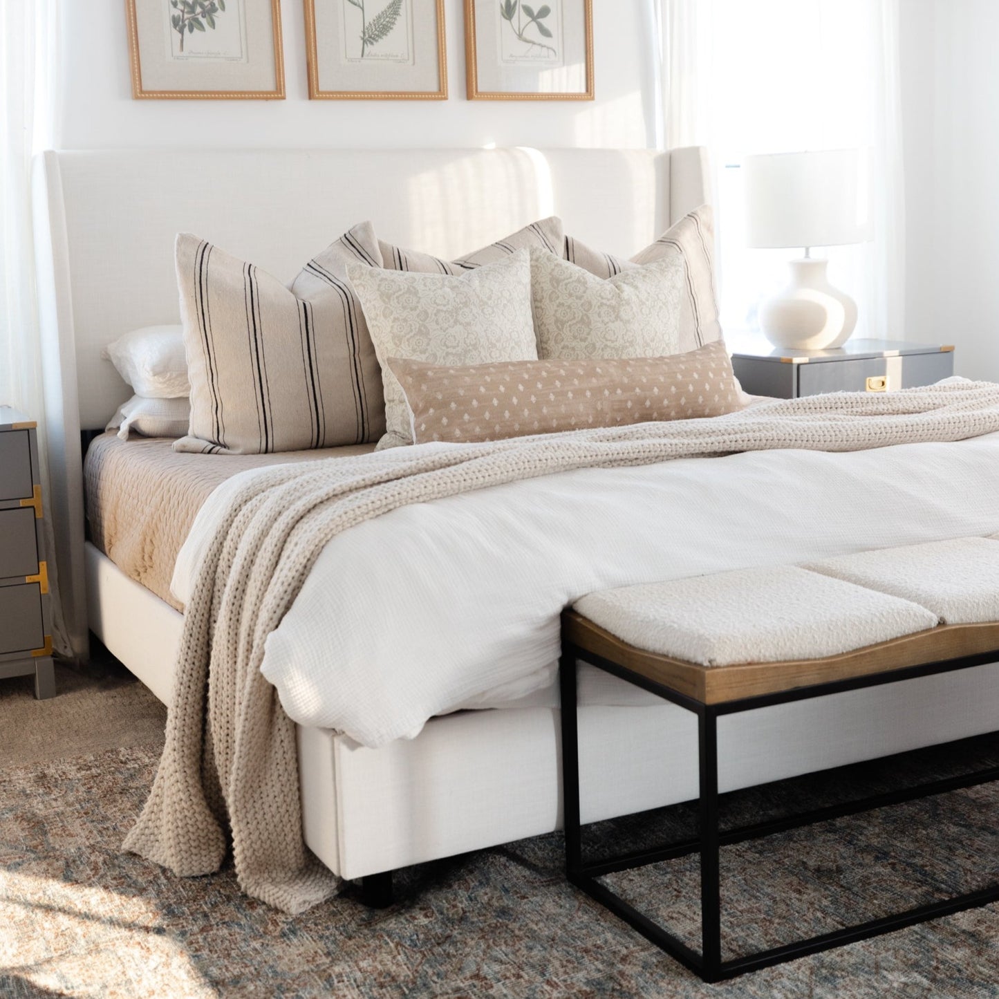 Striped and patterned lumbar pillows in neutral tones arranged on a bed with white headboard and bedding.