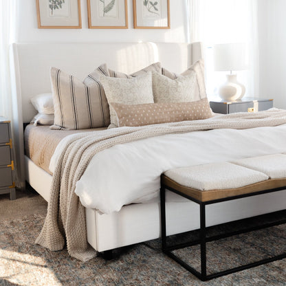 Striped and patterned lumbar pillows in neutral tones arranged on a bed with white headboard and bedding.