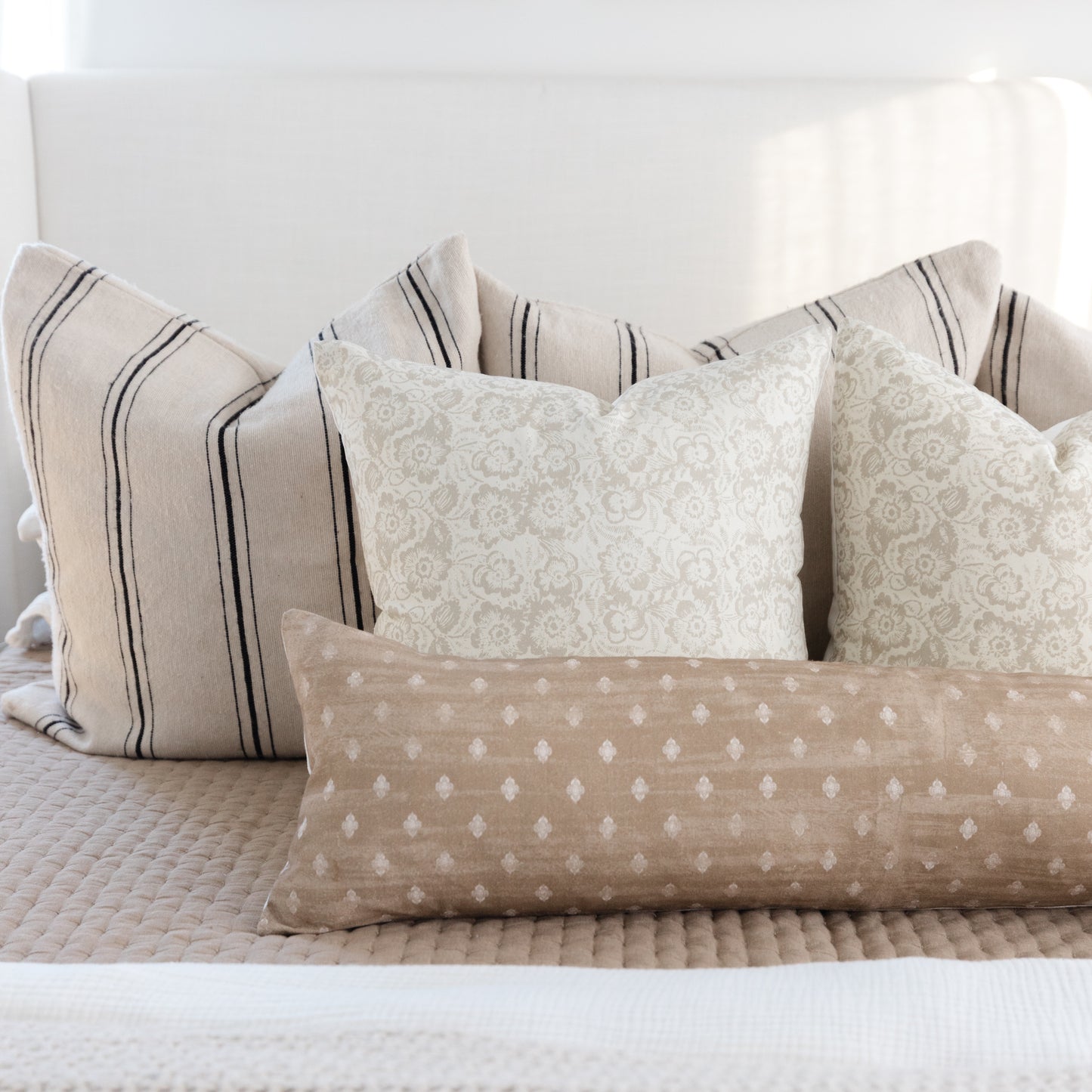 Rectangular lumbar pillow in tan linen with white diamond pattern, displayed with striped and damask accent pillows on a bed.
